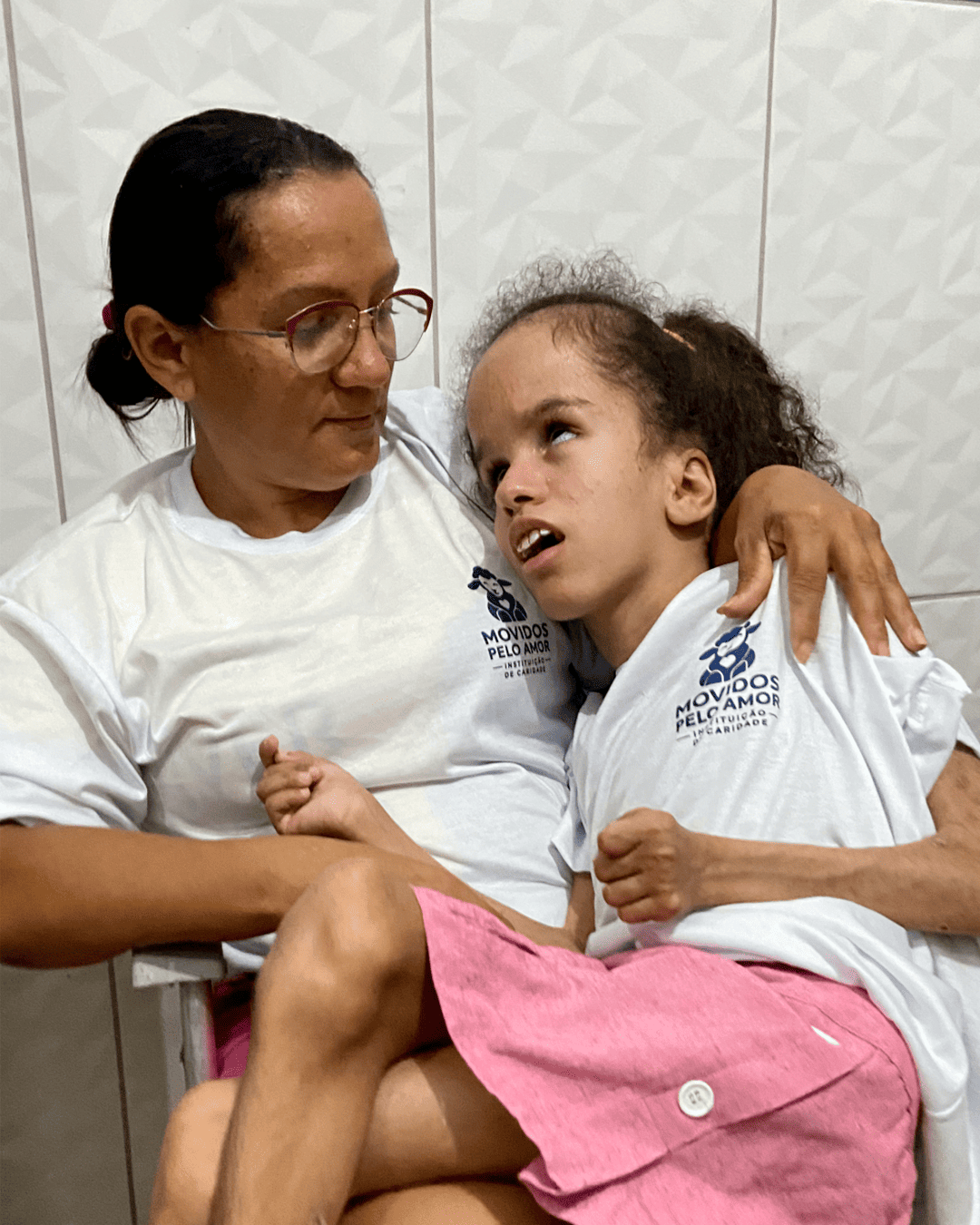 Maria Sônia com Ana Júlia sentada em seu colo dentro de casa